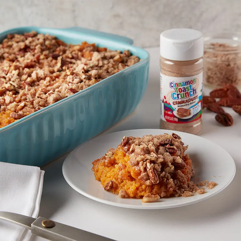Cinnadust™ Sweet Potato Casserole in a large baking tray with a scoop taken out a laid on a plate.