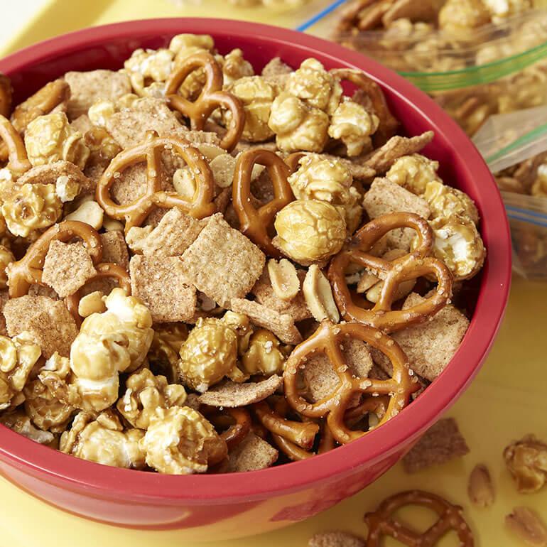 Cinnamon Toast Crunch™ Ball Park Snack Mix in a bowl with more in a zip lock bag behind.