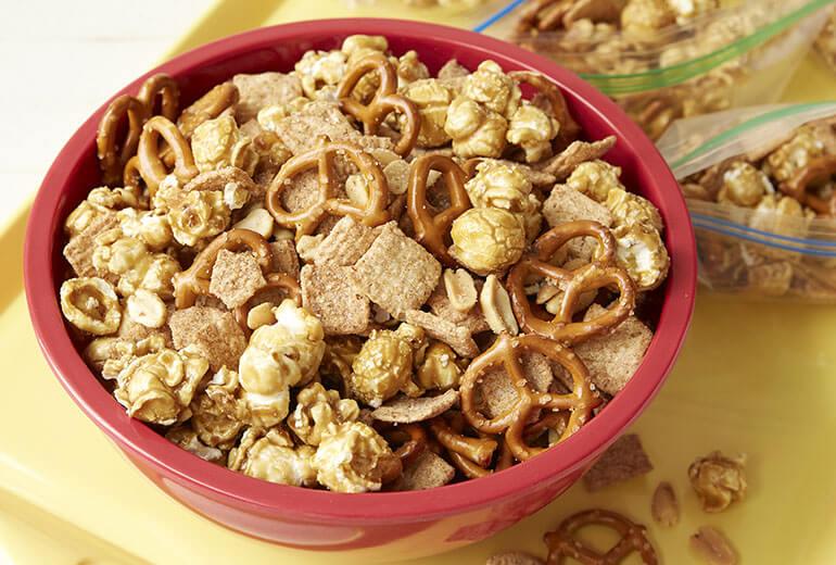 Cinnamon Toast Crunch™ Ball Park Snack Mix in a bowl with more in a zip lock bag behind.