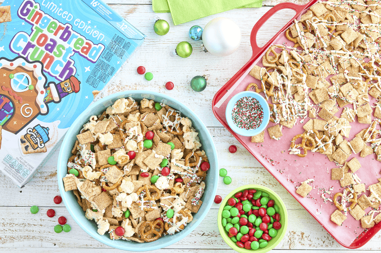 Un bol de Gingerbread Toast Crunch junto a su caja de cereales, así como una bandeja de snacks de cereales y un bol de chocolates confitados. También hay un bol de chispas de colores.