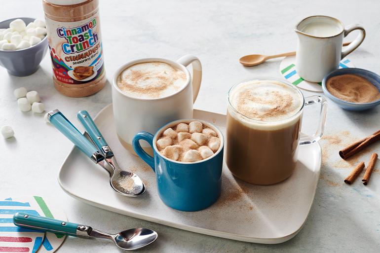 Two cups of Café au Lait with Cinnadust™ on a white serving plate with a cup of marshmallow between the two cups.