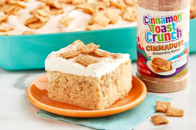 A slice of Cinnamon Toast Crunch™ Cinnadust™ Tres Leches Cake on a plate with a jar of Cinnadust™ beside it.