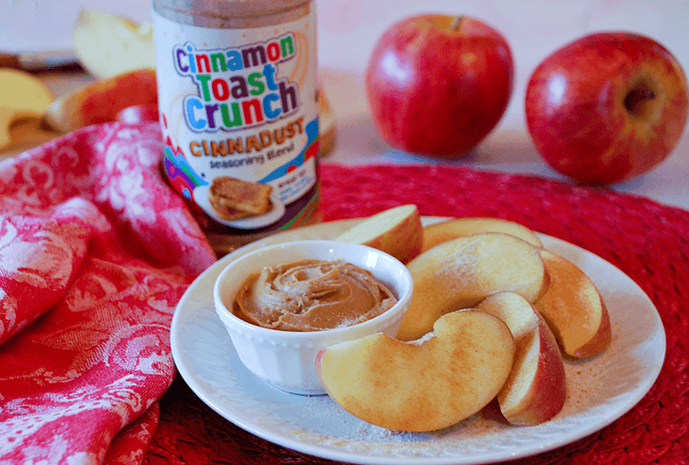 Cinnadust™ Peanut Butter and Apples on a plate with the peanut butter contained to a small pot and behind is a jar of Cinnadust™.