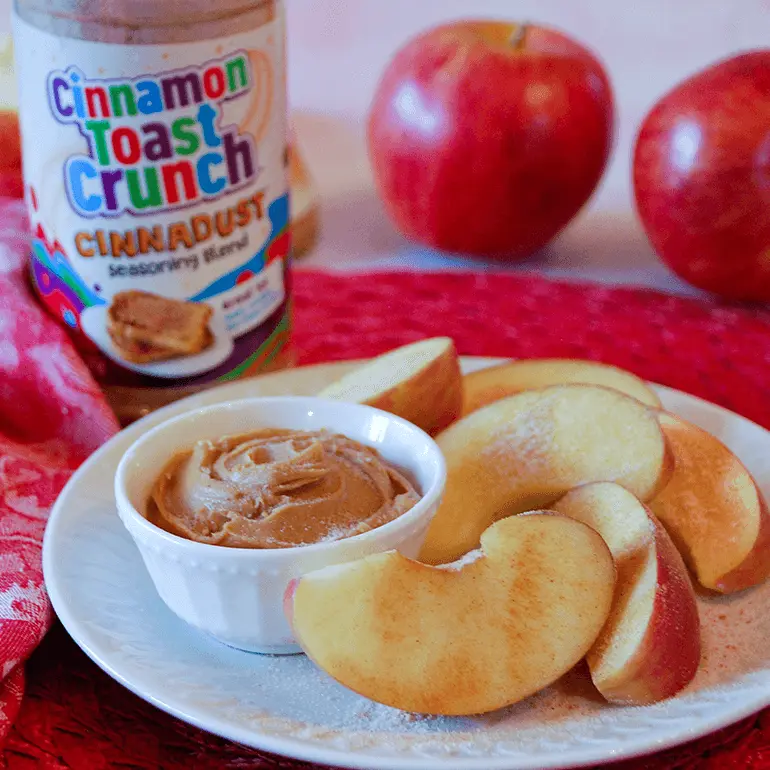 Cinnadust™ Peanut Butter and Apples on a plate with the peanut butter contained to a small pot and behind is a jar of Cinnadust™.