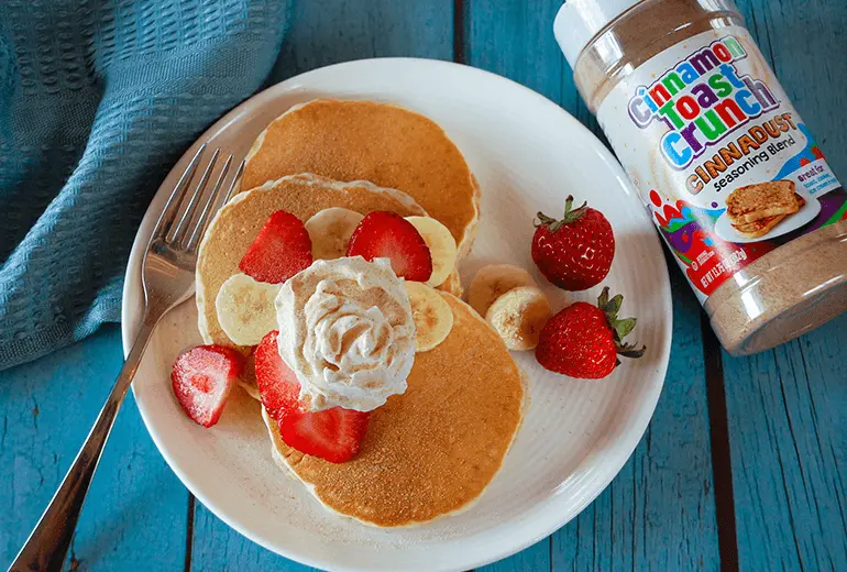 Fluffy Cinnadust™ Pancakes with cream and fresh fruit next to a jar of Cinnadust™.