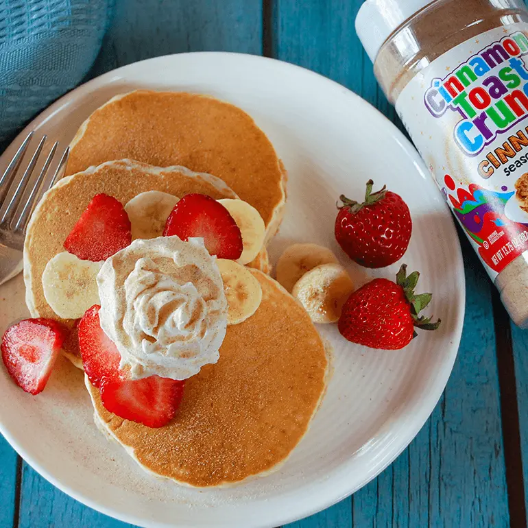 Fluffy Cinnadust™ Pancakes with cream and fresh fruit next to a jar of Cinnadust™.