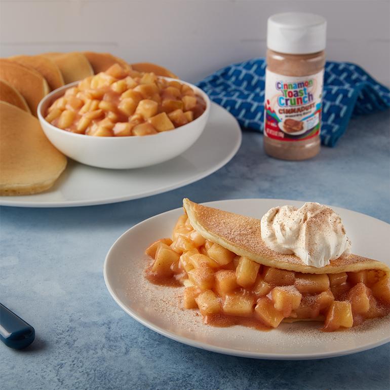 Cinnadust™ Apple Pie Pancakes on a plate in the foreground, behind sits another plate with apple pie filling and more pancakes.