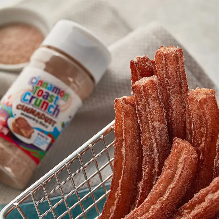 Cinnadust™ Churros in a metal basket with a jar of Cinnadust™ beside it.