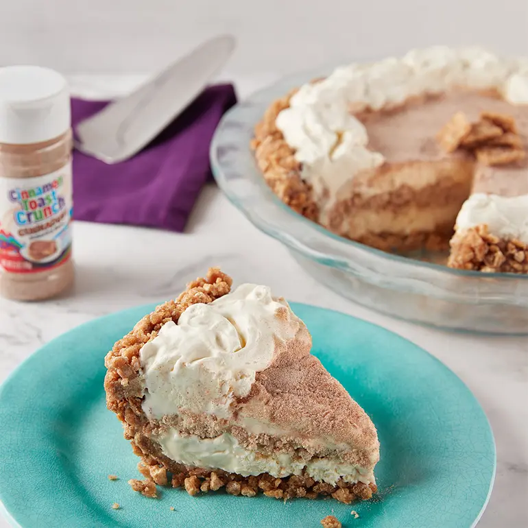 A slice of Cinnamon Toast Crunch™ Ice Cream Pie on a plate with more of the pie behind it.