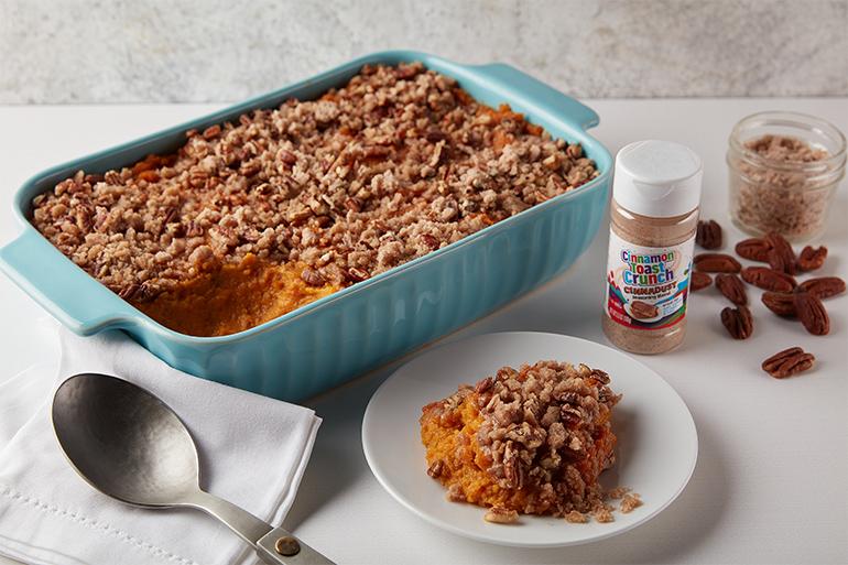Cinnadust™ Sweet Potato Casserole in a large baking tray with a scoop taken out a laid on a plate.