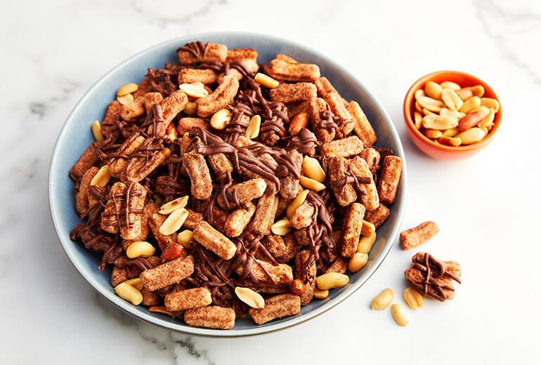 Chile-Chocolate Churros Snack Mix in a large bowl with peanuts in a smaller bowl next to it.