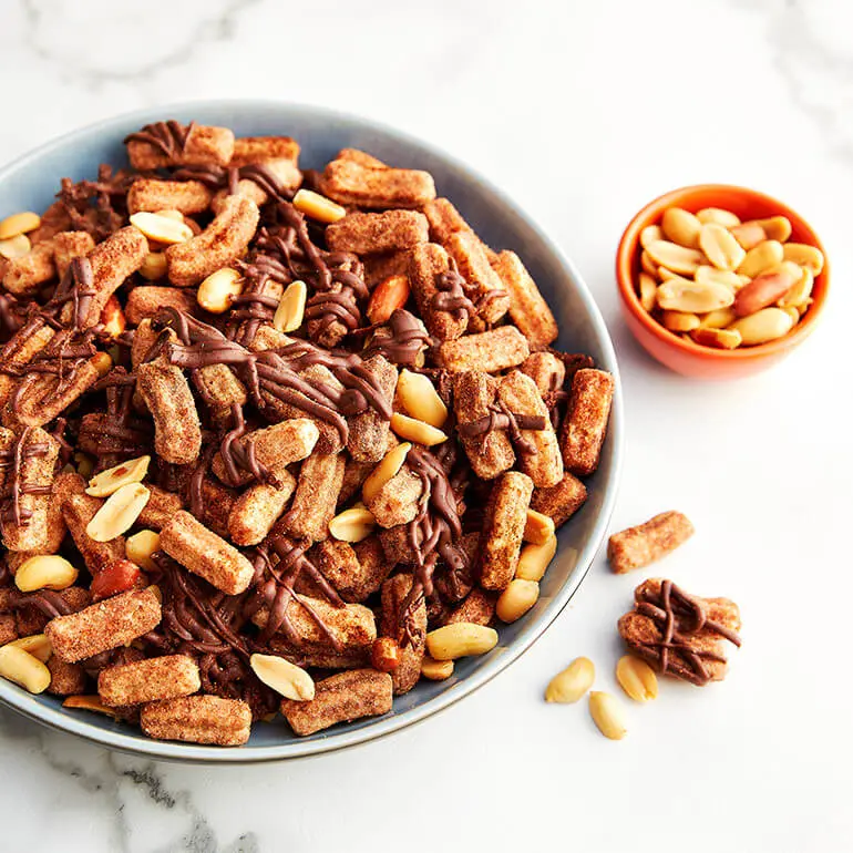 Chile-Chocolate Churros Snack Mix in a large bowl with peanuts in a smaller bowl next to it.