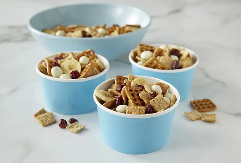 Fruit & Cinnamon Snack Mix filling three separate cardboard cups and a bowl behind them.