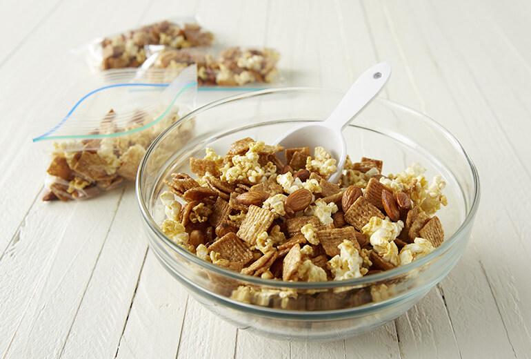 Glazed Cinnamon and Popcorn Snack Mix in a bowl with plastic resealable bags of the mix behind it.