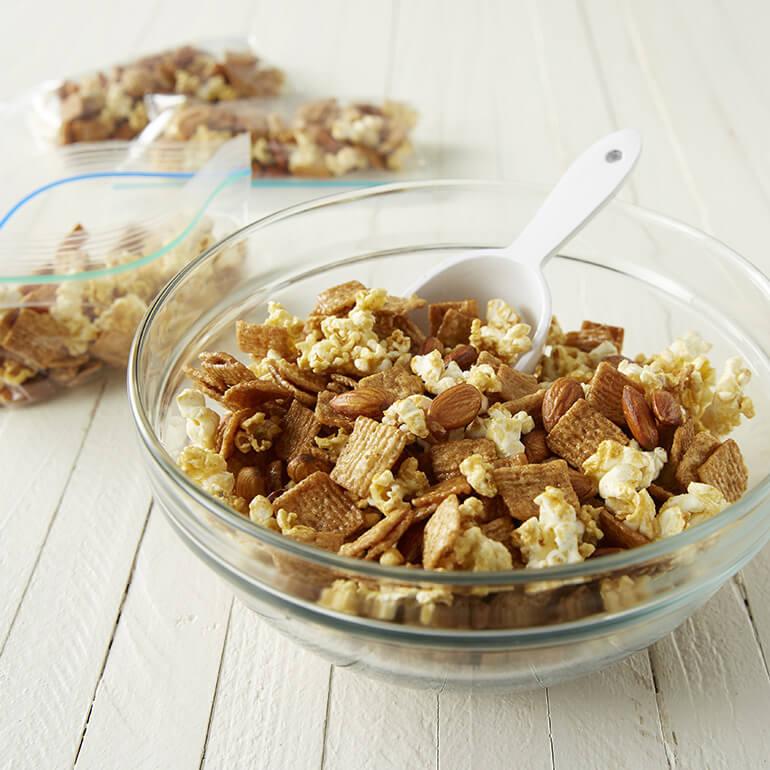 Glazed Cinnamon and Popcorn Snack Mix in a bowl with plastic resealable bags of the mix behind it.