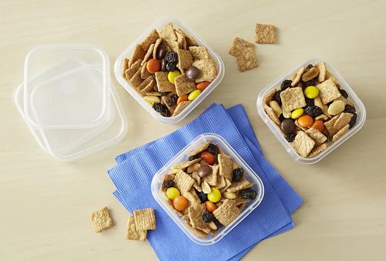 An overhead shot of Cinnamon Gorp Snack Mix split between three Tupperware with the lids off.