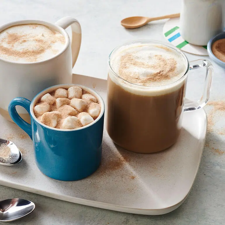 Two cups of Café au Lait with Cinnadust™ on a white serving plate topped with froth and marshmallows.