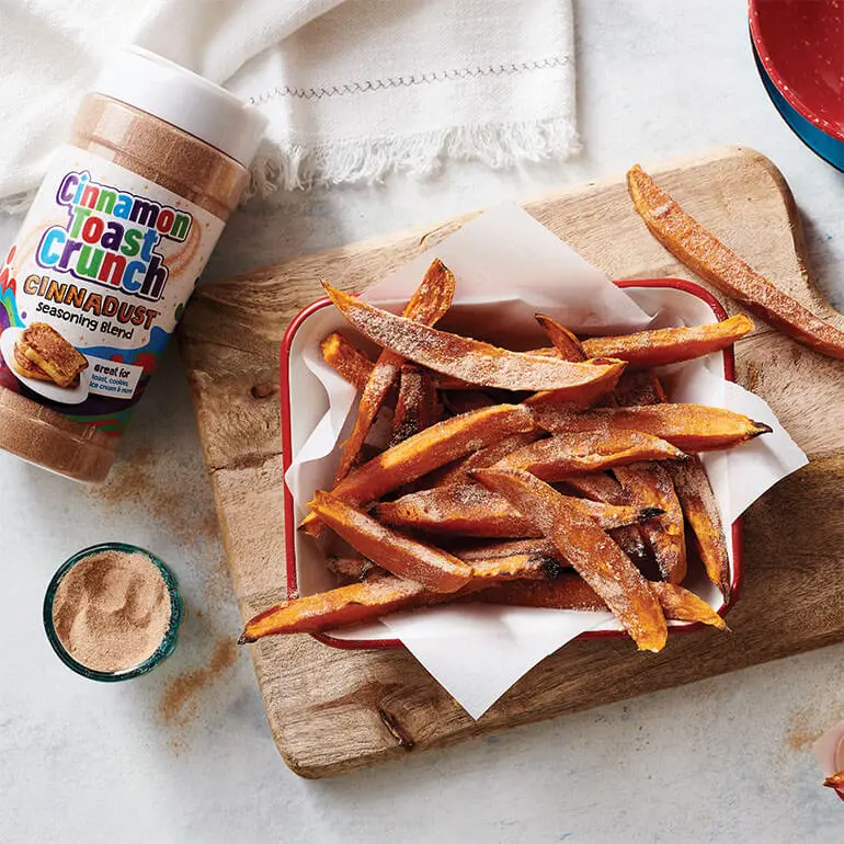 Roasted Sweet Potato Fries with Cinnadust™ on a wooden serving board with a jar of Cinnadust™ beside it.