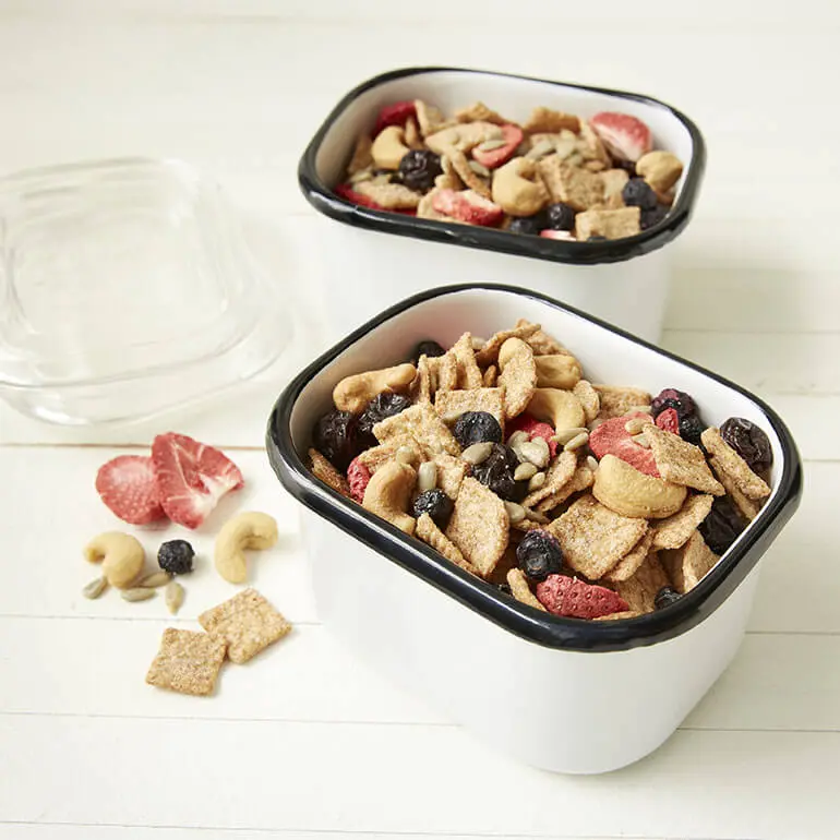 Two cups of Cinnamon Toast Crunch™ Fruit, Nuts and Seeds Mix on white wooden surface.