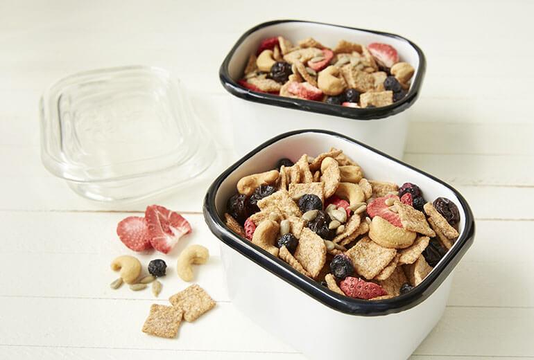 Two cups of Cinnamon Toast Crunch™ Fruit, Nuts and Seeds Mix on white wooden surface.