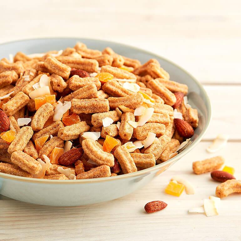 Mango and Coconut Churros Cereal Snack Mix in a grey ceramic bowl on a wooden surface.