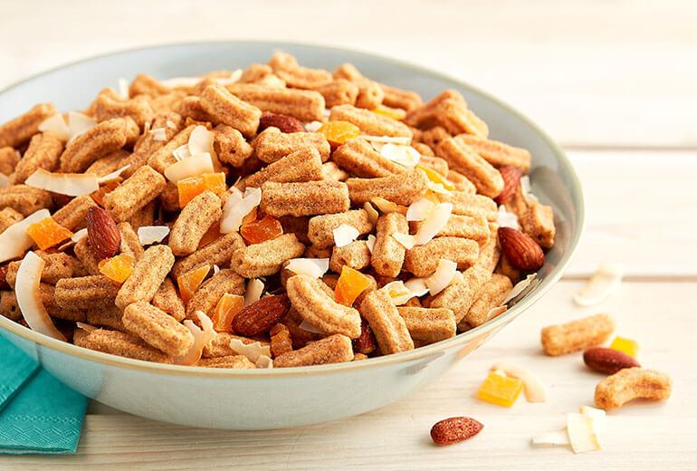 Mango and Coconut Churros Cereal Snack Mix in a grey ceramic bowl on a wooden surface.