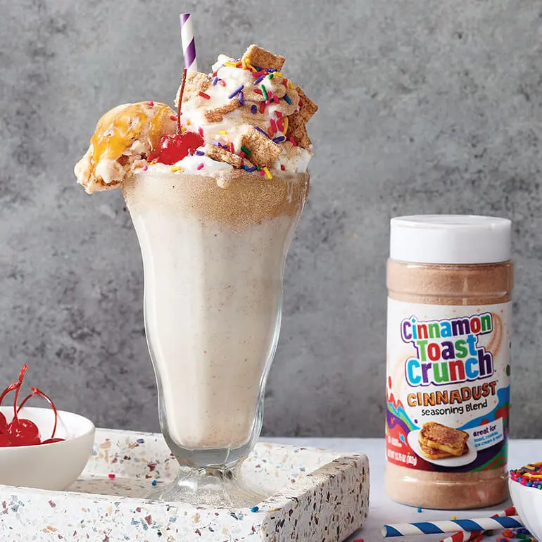 A Cinnamon Toast Crunch Cinnadust™ Milkshake with a bowl of glazed cherries and a jar of Cinnadust™.