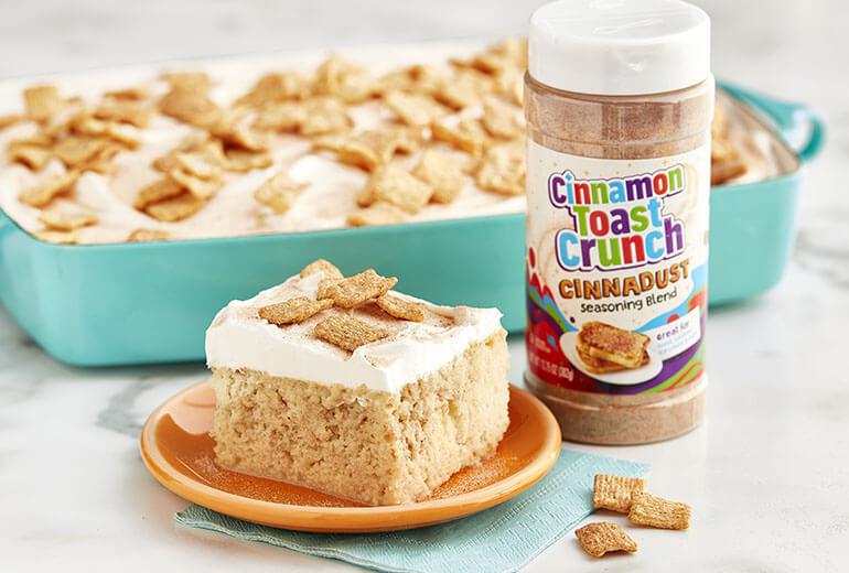 A slice of Cinnamon Toast Crunch™ Cinnadust™ Tres Leches Cake on a plate with a jar of Cinnadust™ beside it.