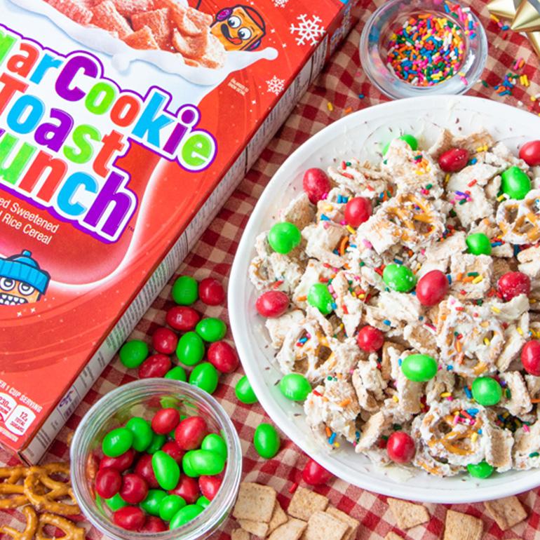 A bowl of the Sugar Cookie Toast Crunch™ Snack Mix surrounded by Christmas decorations and ingredients.
