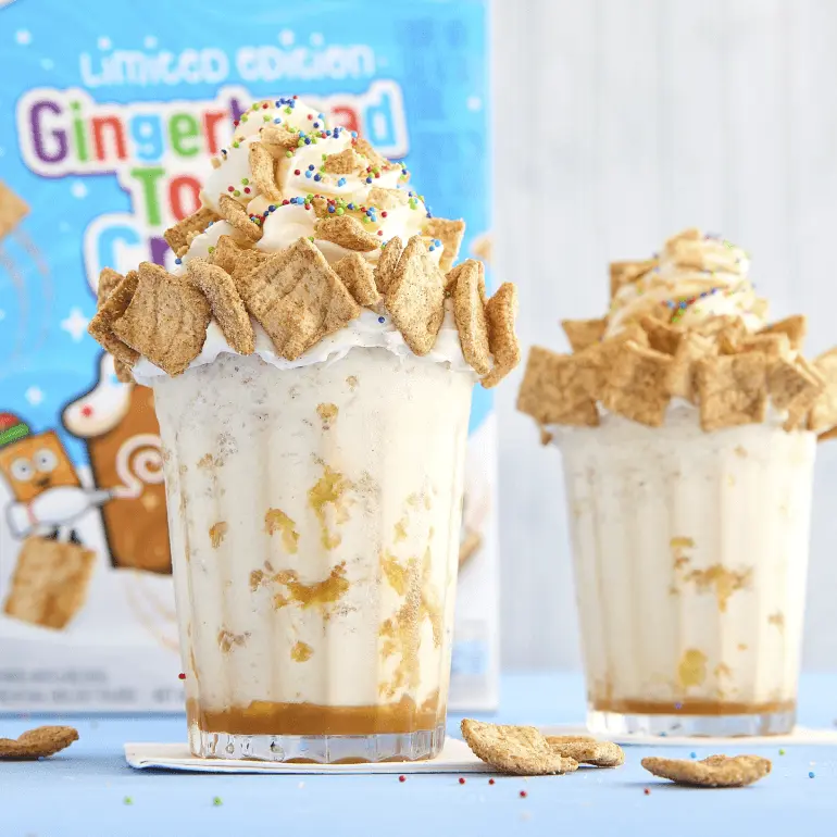 Two glasses of Gingerbread Toast Crunch Cereal Milk Shakes with Gingerbread Toast Crunch cereal box in the background.